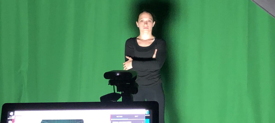Performer standing in front of green screen with a camera pointed at her