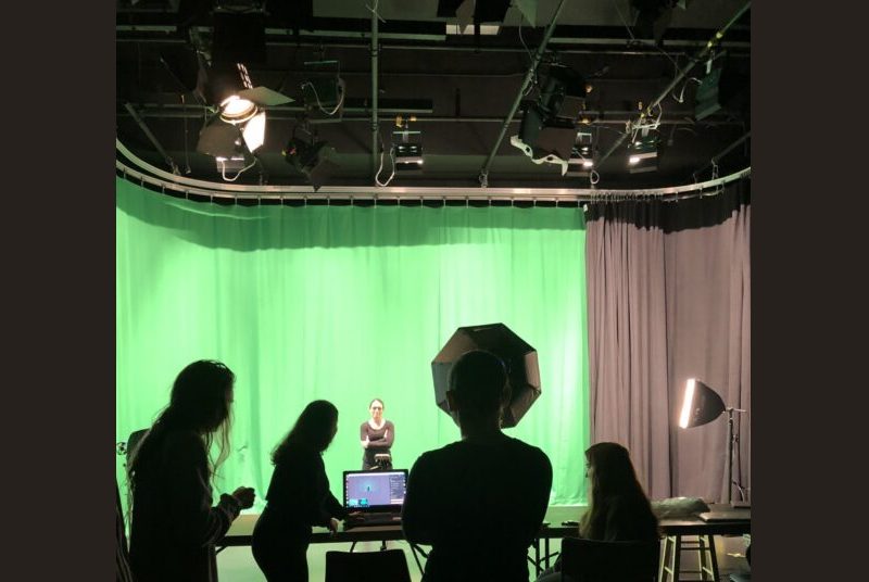 Performer standing in front of camera with students behind camera looking at a laptop screen