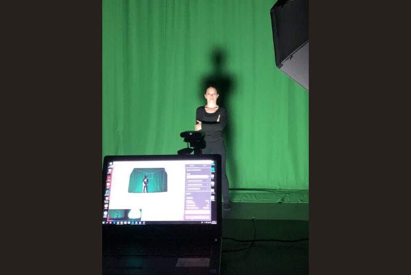 Performer standing in front of green screen with a camera pointed at her