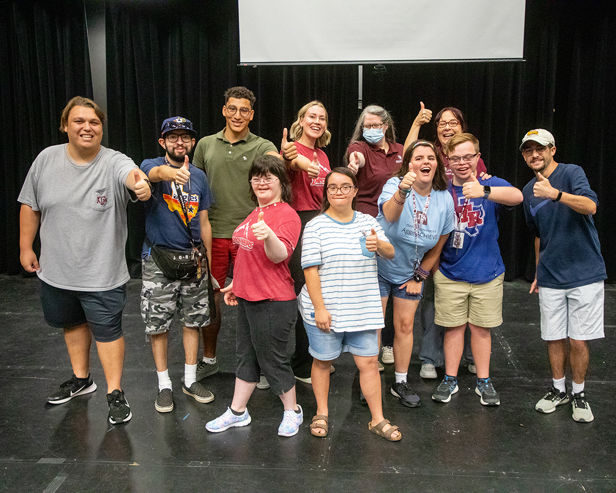 A group of people in an improvisational workshop smile and pose for the camera.