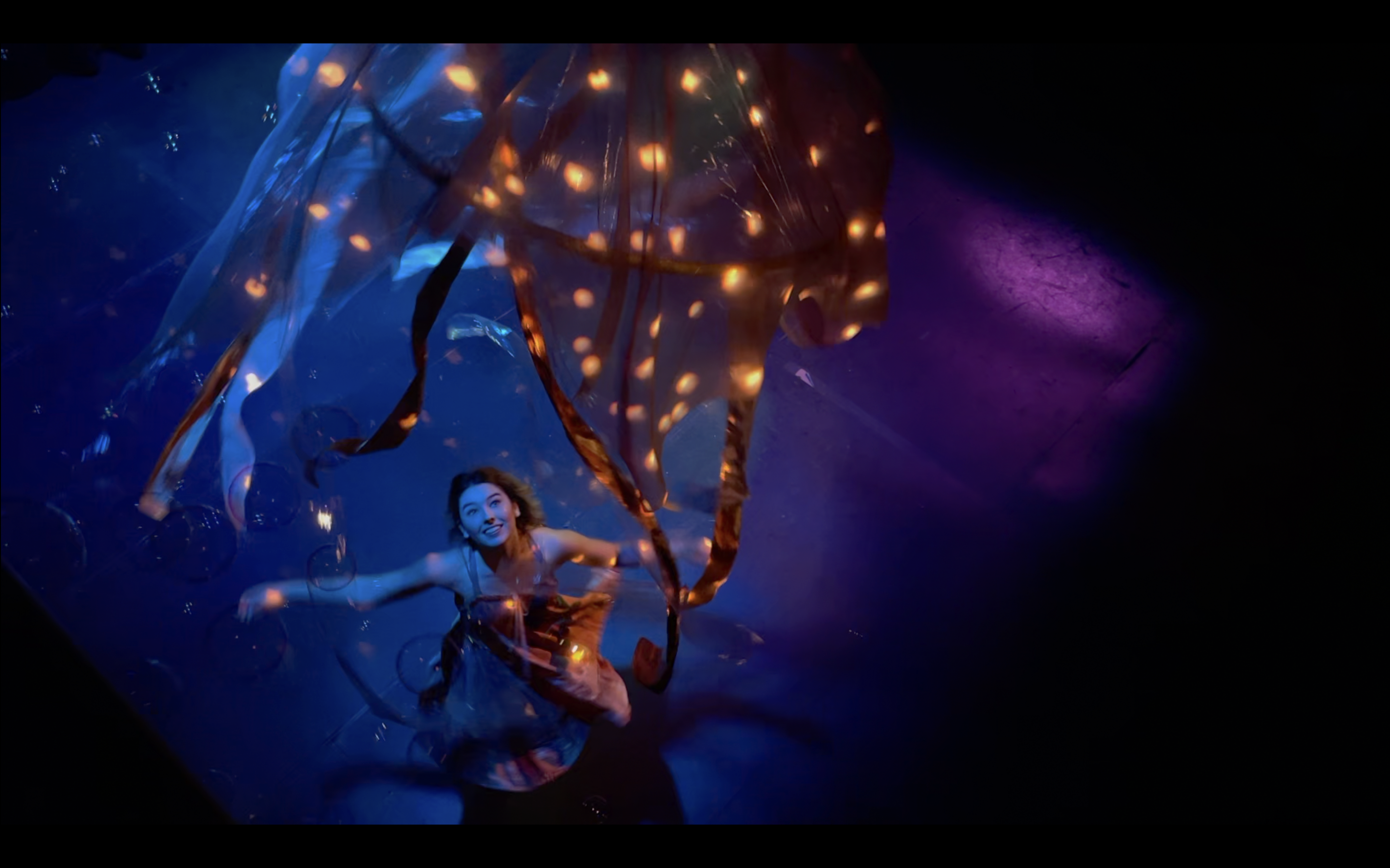 A performer onstage reaches out and grasps a ribbon suspended from the ceiling.