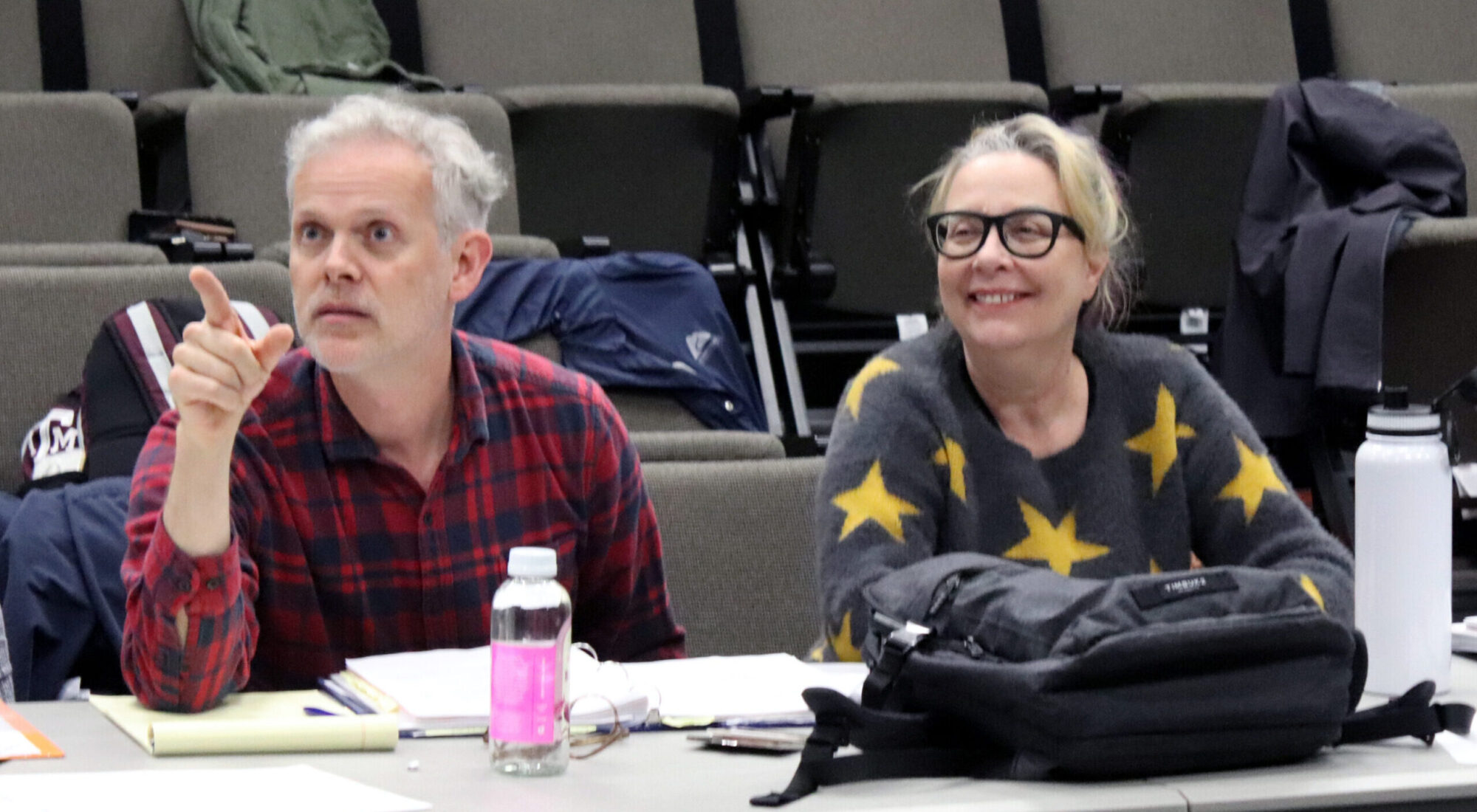 Two theater directors are seated at a table, instructing students.