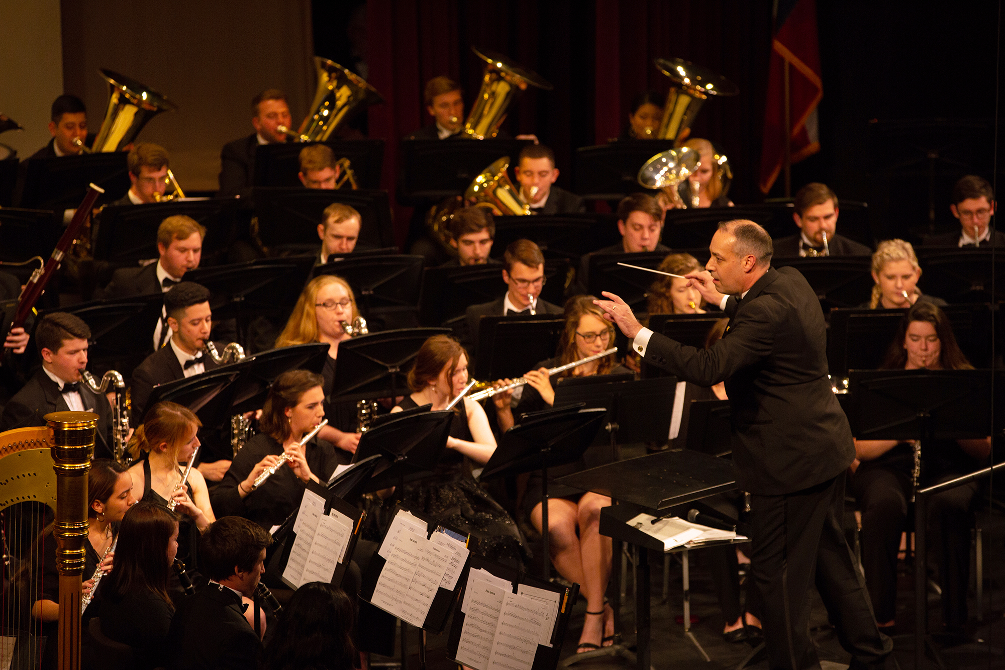 An orchestra conductor gestures in front of a group of student musicians as they perform.