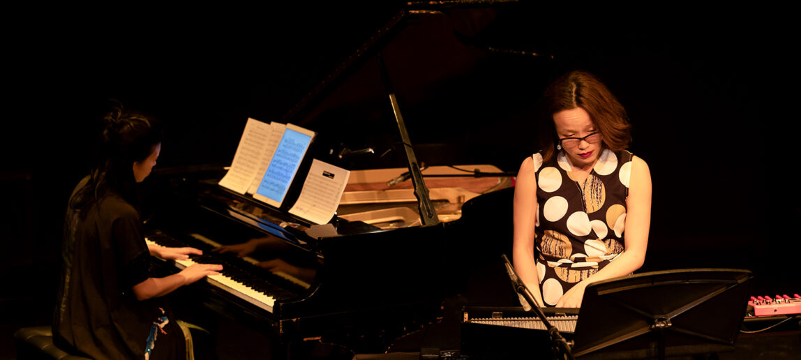 Two performers near instruments on a black stage
