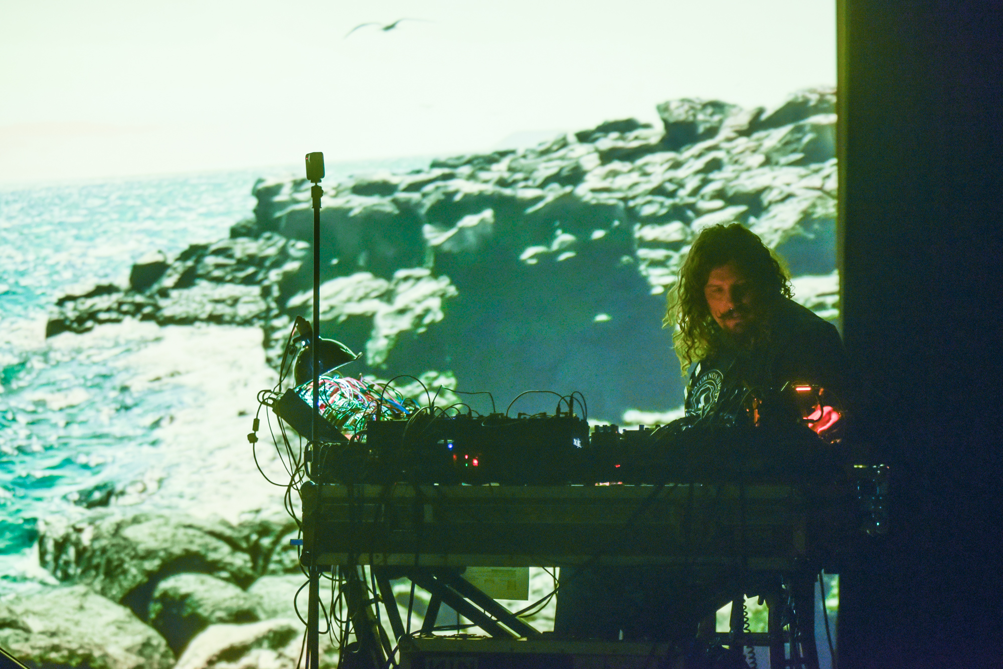 An artist using electronic equipment performs in front of an illuminated backdrop.