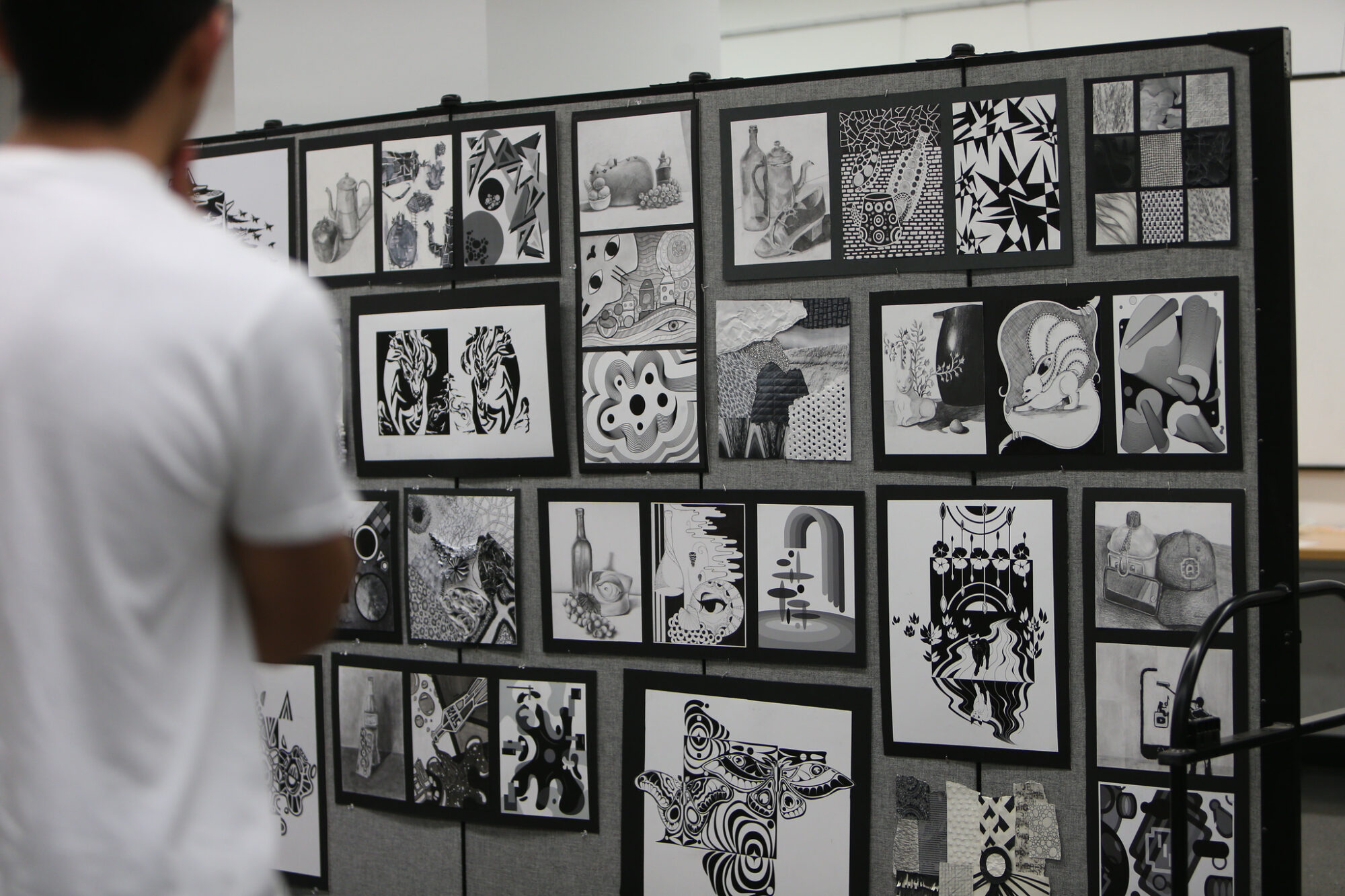 A college student stands before a display of black-and-white artwork.