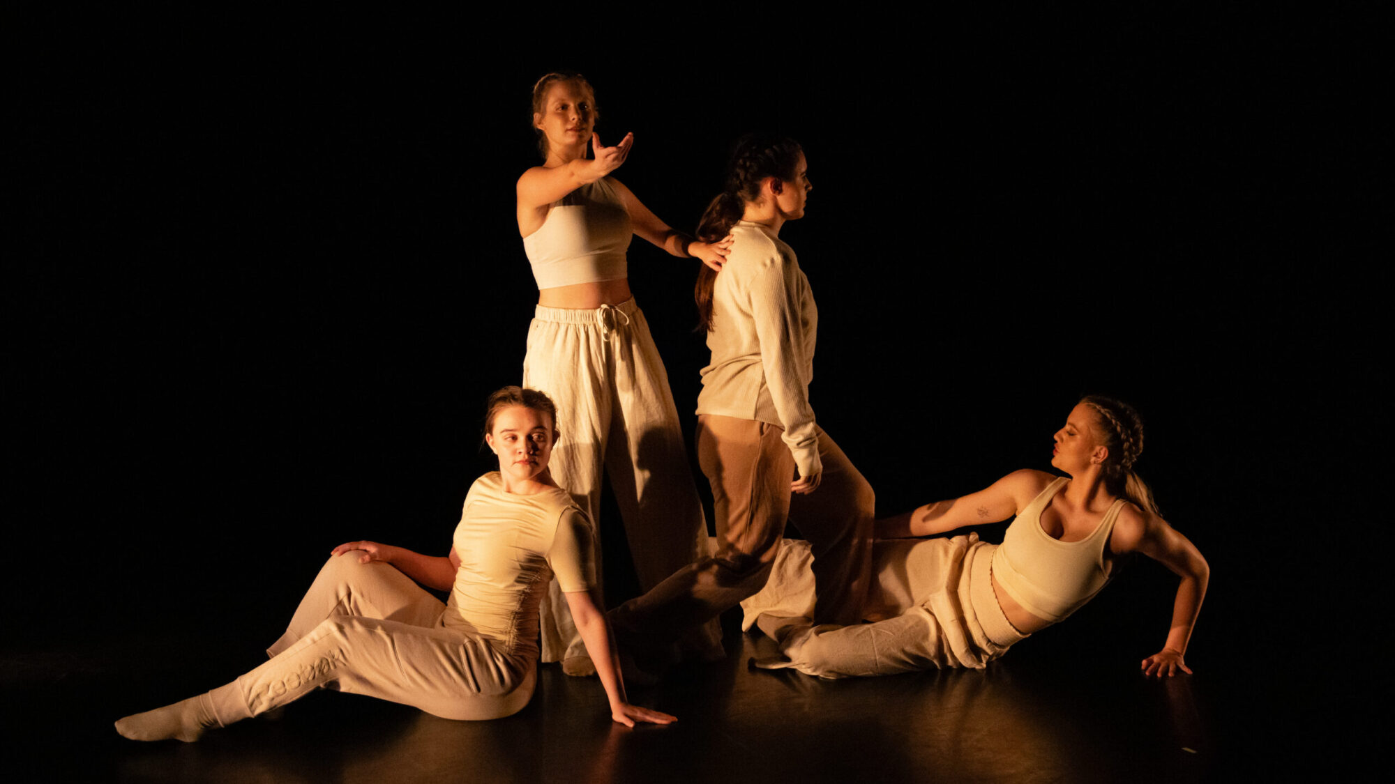 Four women in cream suits dancing against a black background
