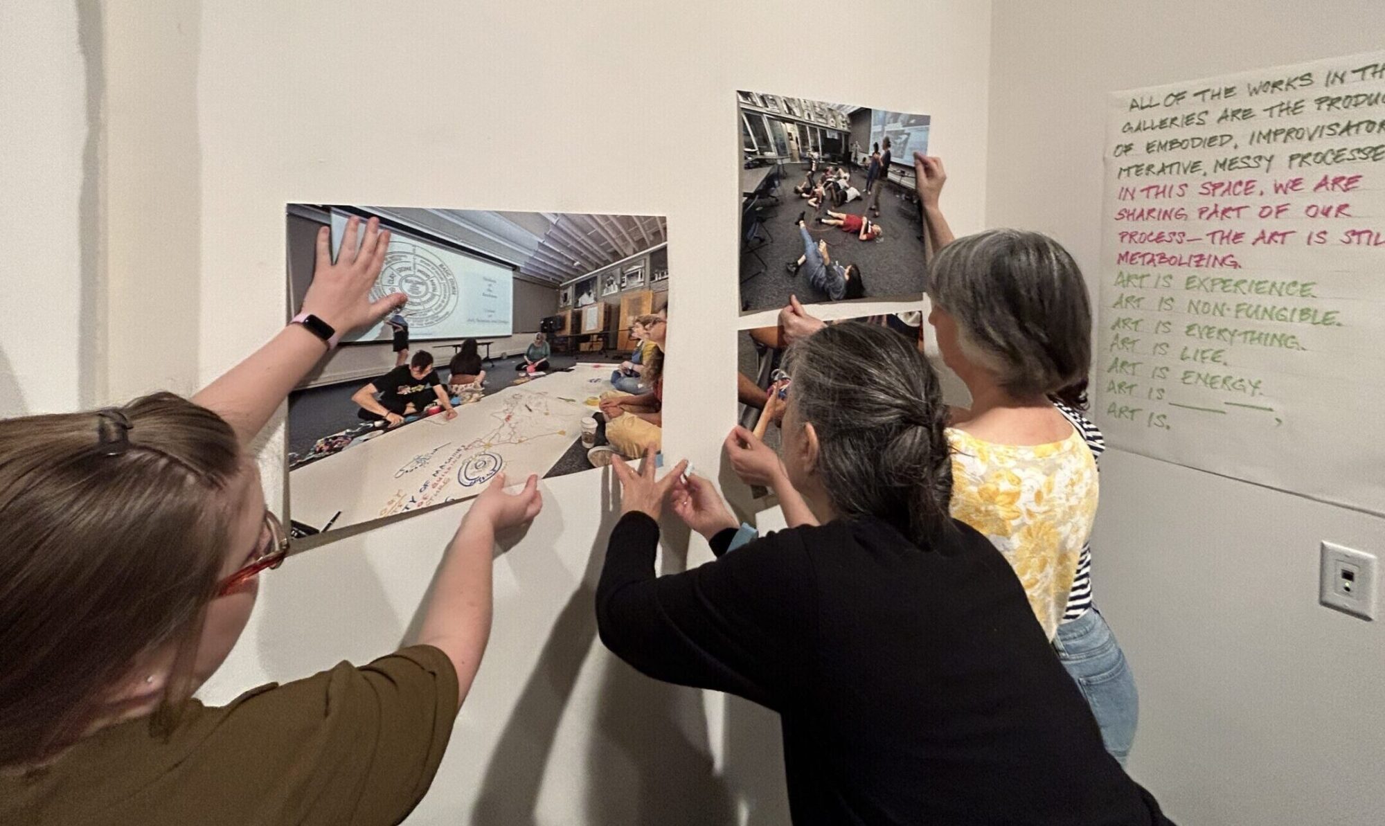 Three people attach photos to a white wall.