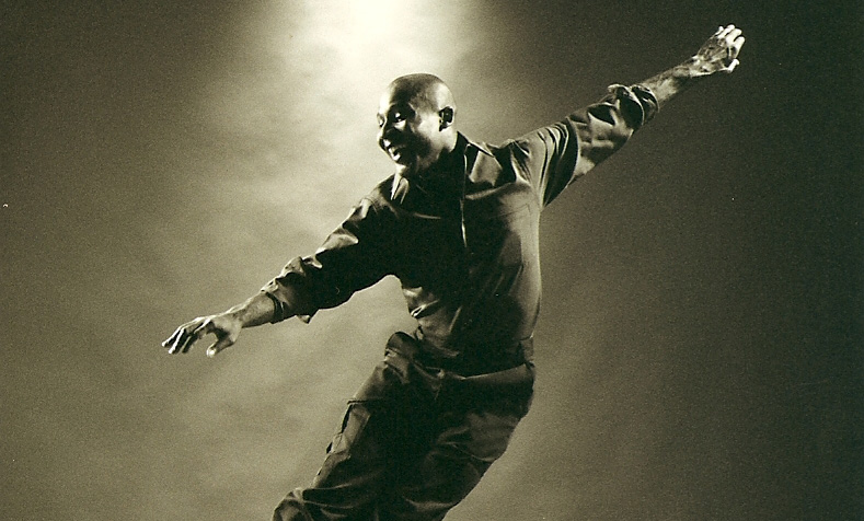 A dancer is shown in midair, with his feet together and his arms extended outward.
