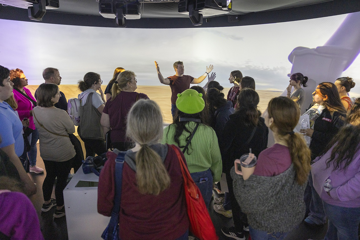 Students and family members gather in an immersive 360-degree screen environment as they listen to a presentation.