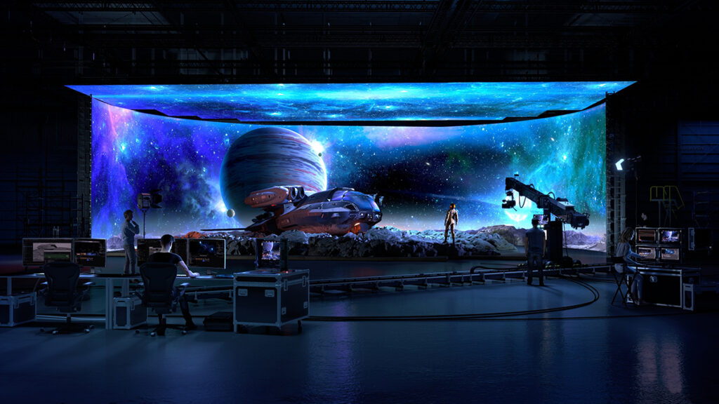 A virtual production stage is shown, with images of outer space. A starship and an actor are in front of the screen. In the foreground are people working on filming the scene.
