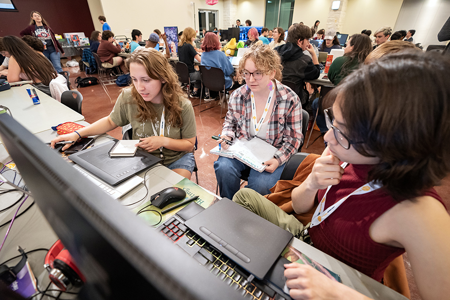 Three college students look at a computer screen as they discuss their work in a video game jam.