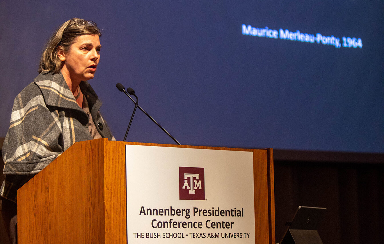 A college professor stands at a podium, giving a presentation.