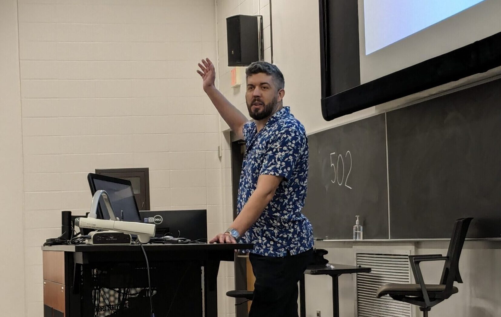 A professional in the music industry stands behind a desk in a college classroom, speaking to students.