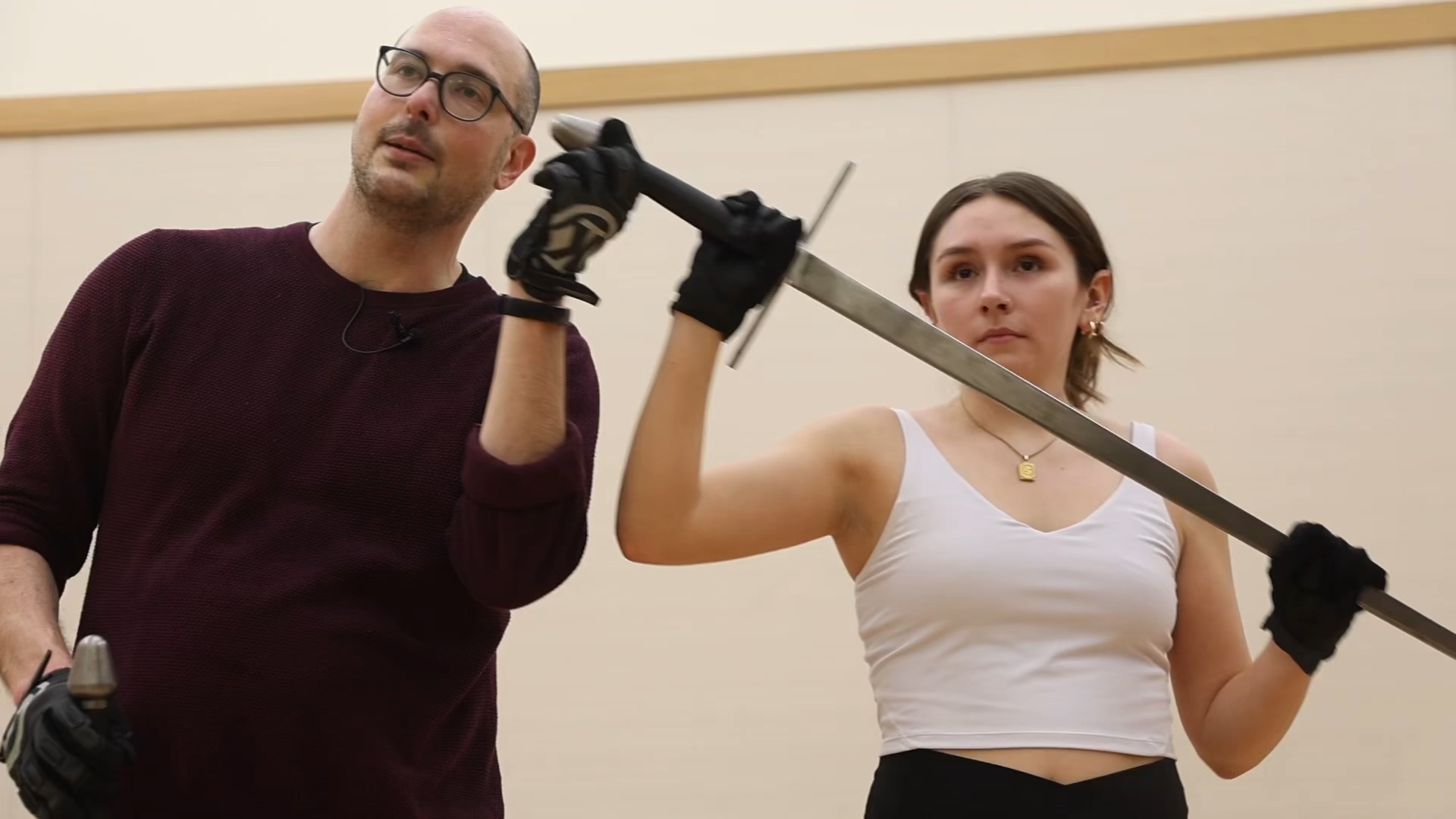 A college student holds a sword in a theatre training exercise, with her professor standing to her right.