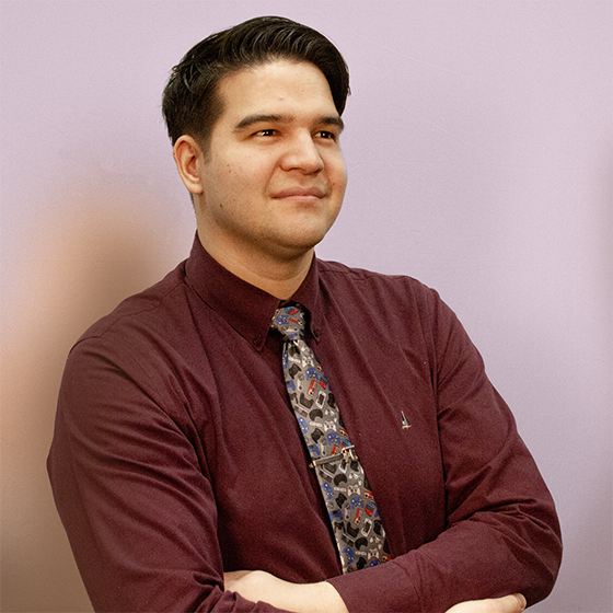 A main standing in front of a gray background, looking to the side with arms crossed.