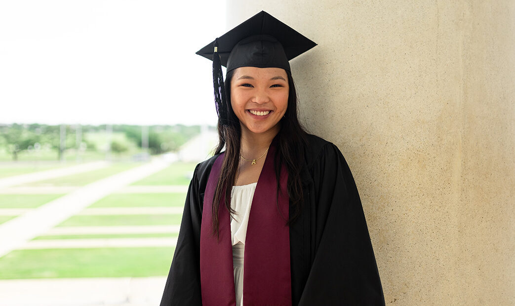 A college student in a graduation cap and gown and a maroon Texas A&M sash poses for a portrait.