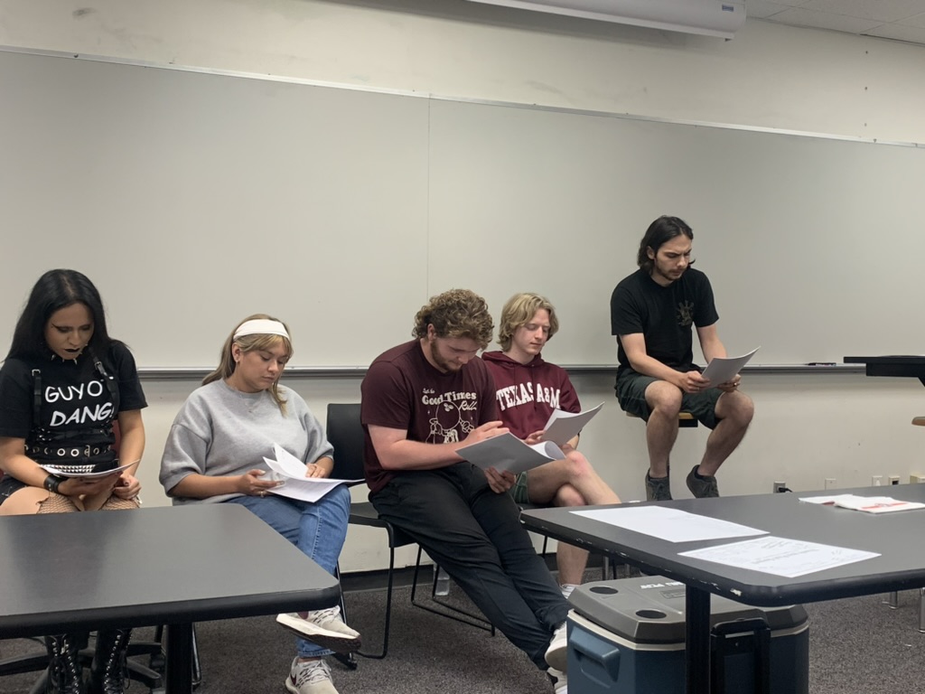 Five students sitting in a classroom in a screenwriting class look at their screenplays.
