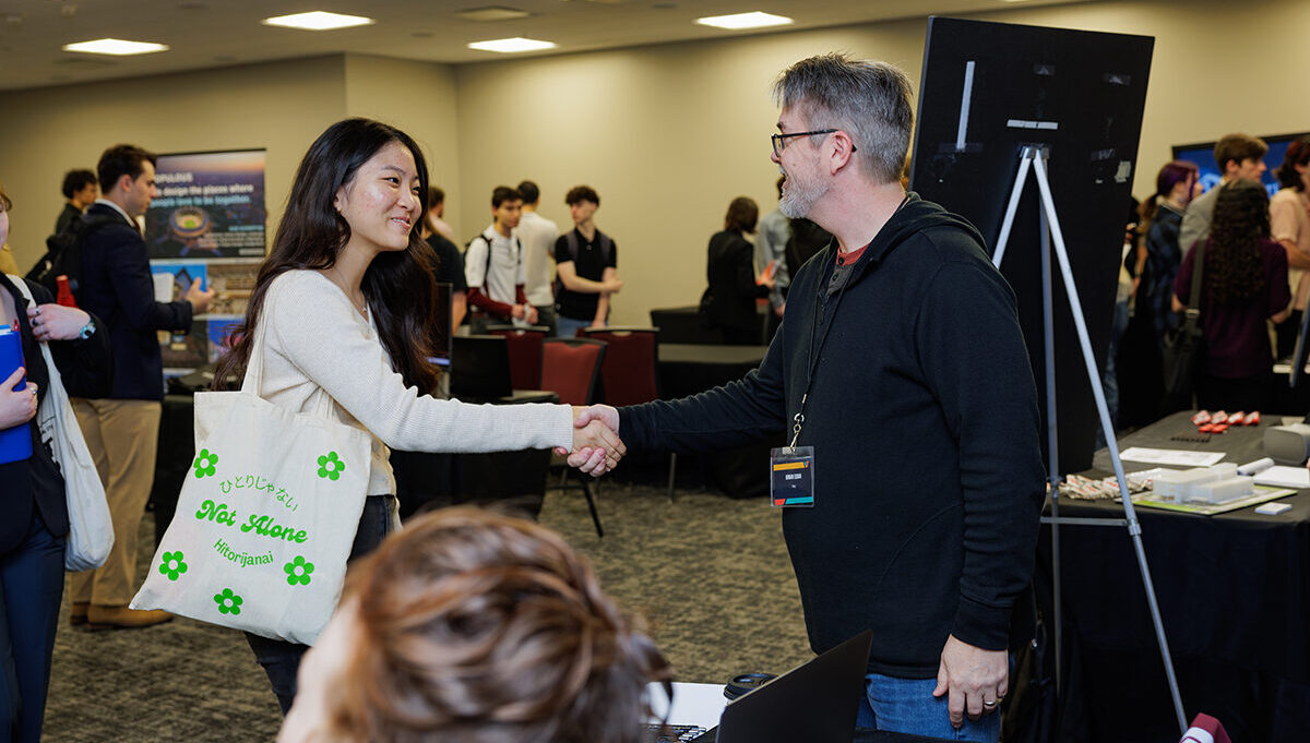 A college student shakes the hand of an industry professional during a career fair.