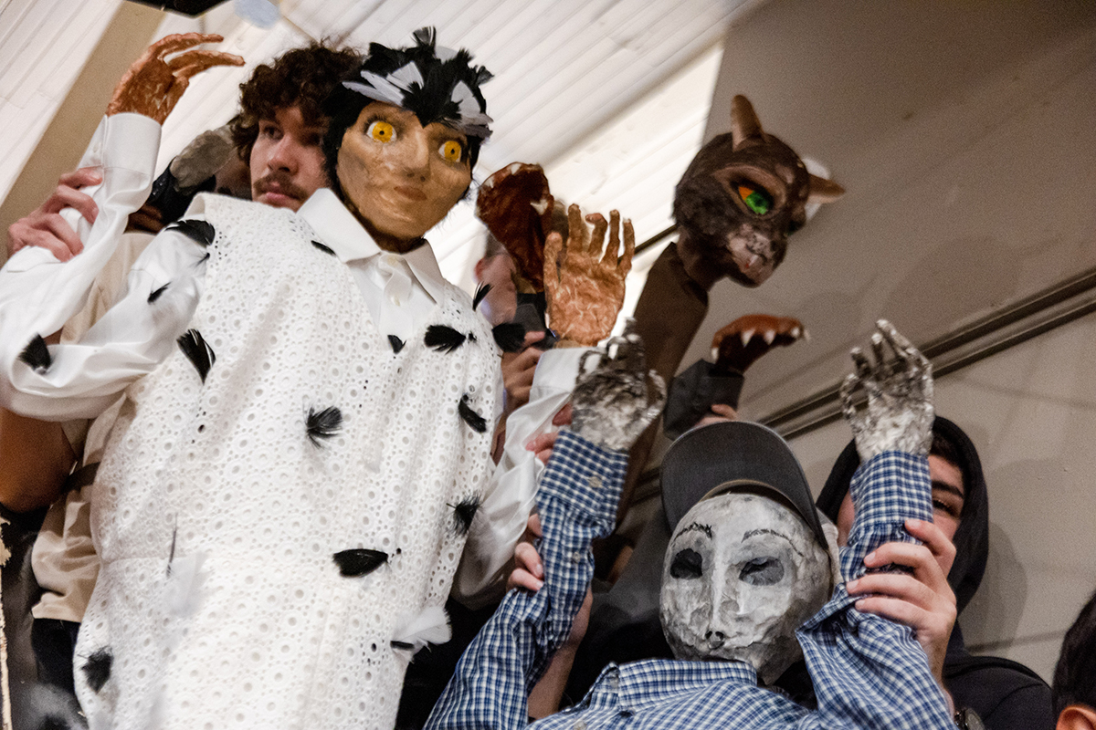 College students are standing on a staircase, holding up puppets they created based on stories of folklore.