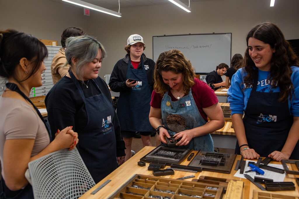 College students smile as a librarian shows them the printing process for hand-setting type.