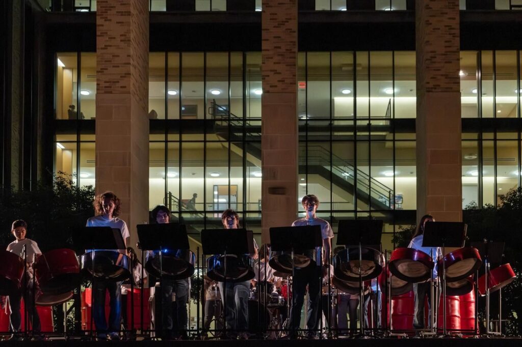 A steel pan ensemble performs an evening concert outside of a university building.