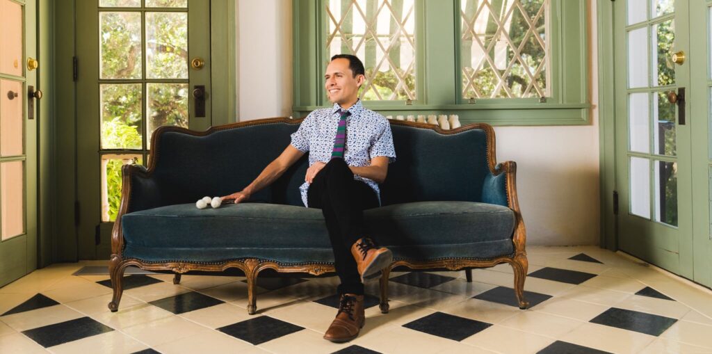 A percussion performer sits on a couch with marimba mallets at his side.