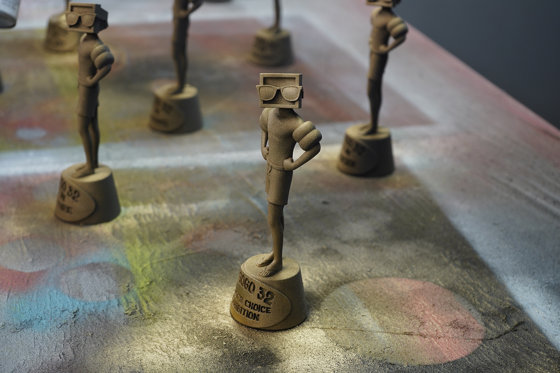 Award statues painted in gold feature a figure with a computer screen for a head, also wearing sunglasses.
