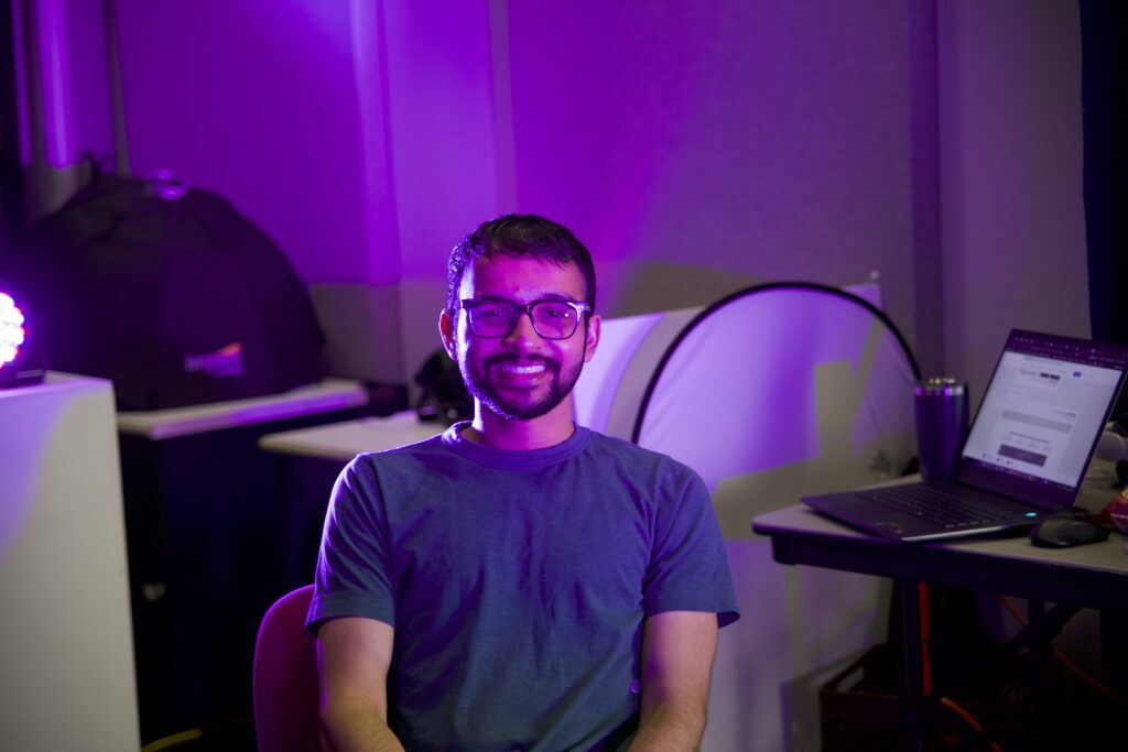 Dhruv Rathod sitting in a room with purple lighting and wearing a blue shirt