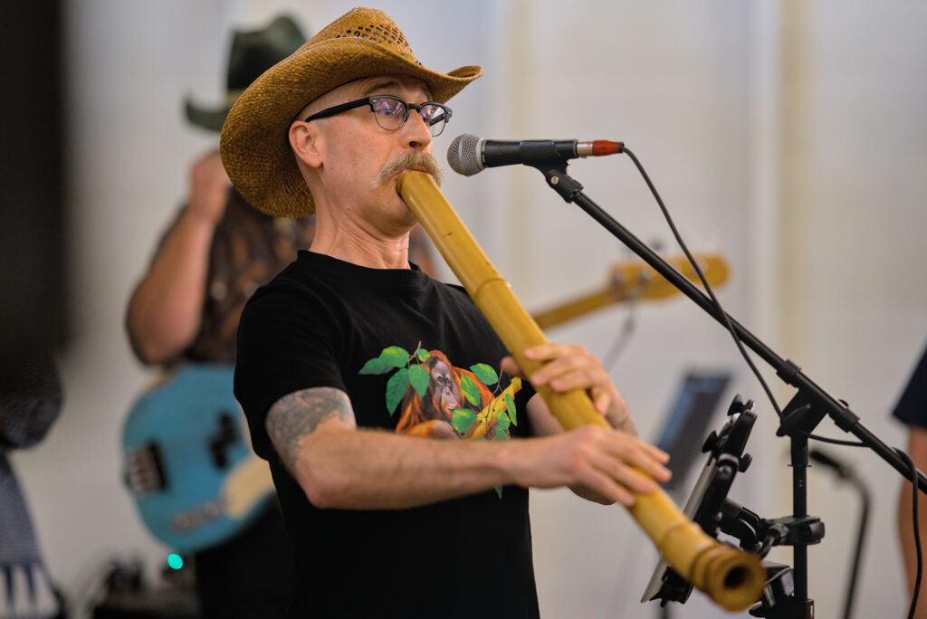 An artist in a cowboy hat performs on the shakuhachi bamboo flute.