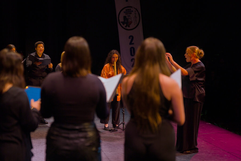 A music professor leads a group of singers in a performance, alongside an artist playing the shakuhachi.