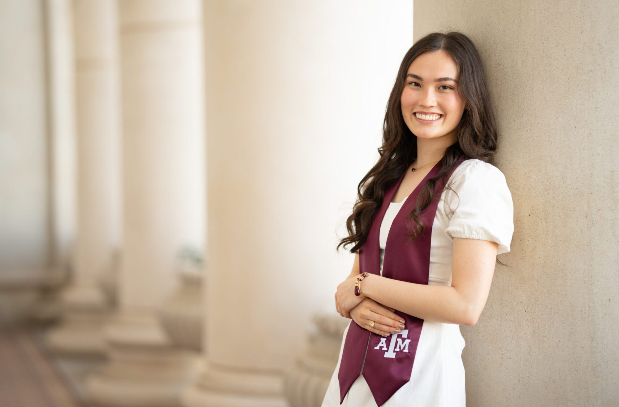 A college student wearing a maroon Texas A&M graduation sash smiles for a portrait.