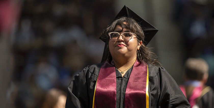 A college student wearing a graduation cap and gown walks the stage on graduation day.