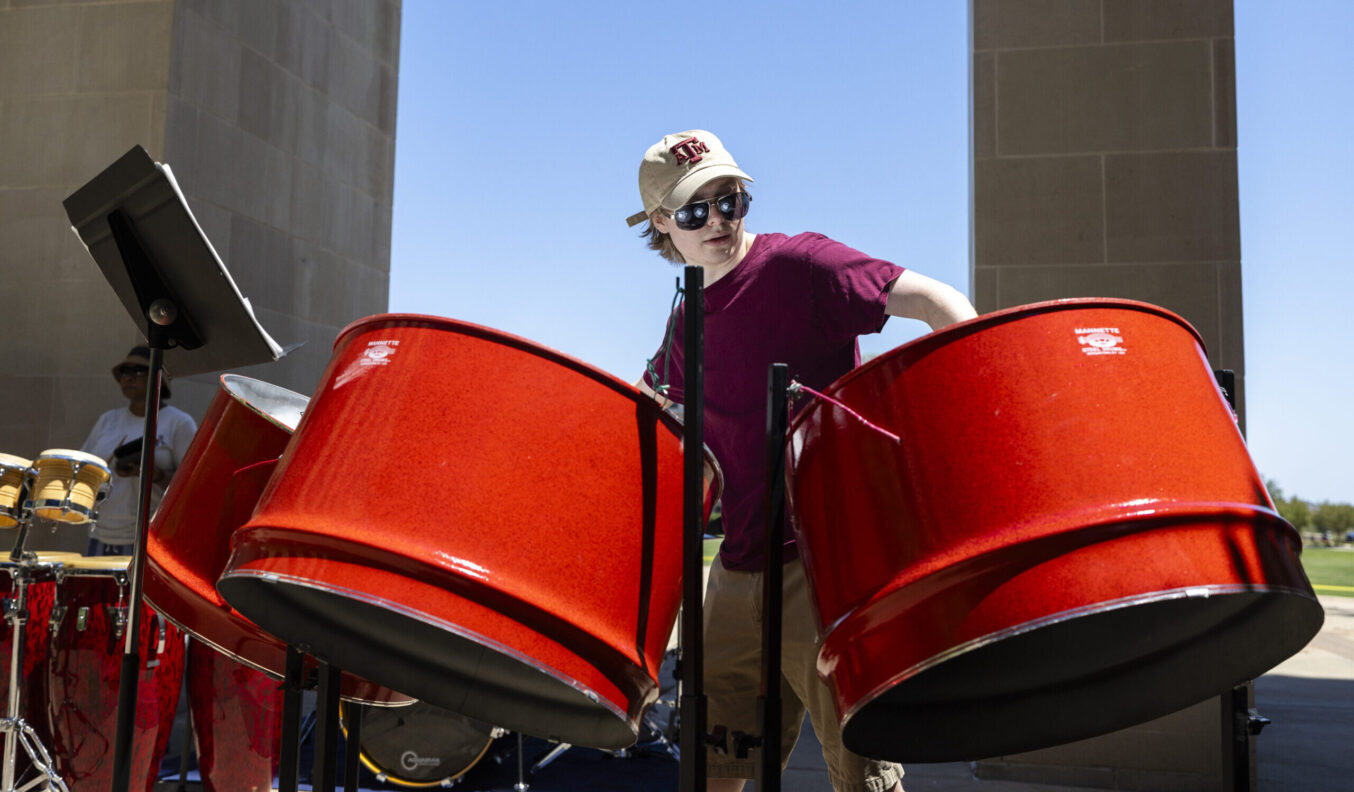 A student performs on steel pan in an outdoor courtyard.