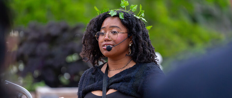 A student wearing a leafy crown speaks into a headset microphone.