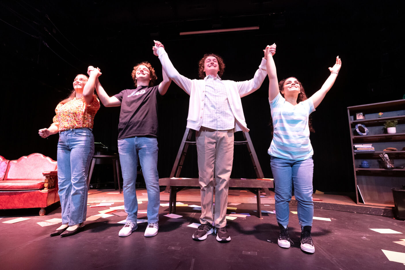 Four college students raise their arms with joined hands at the end of a theater performance.