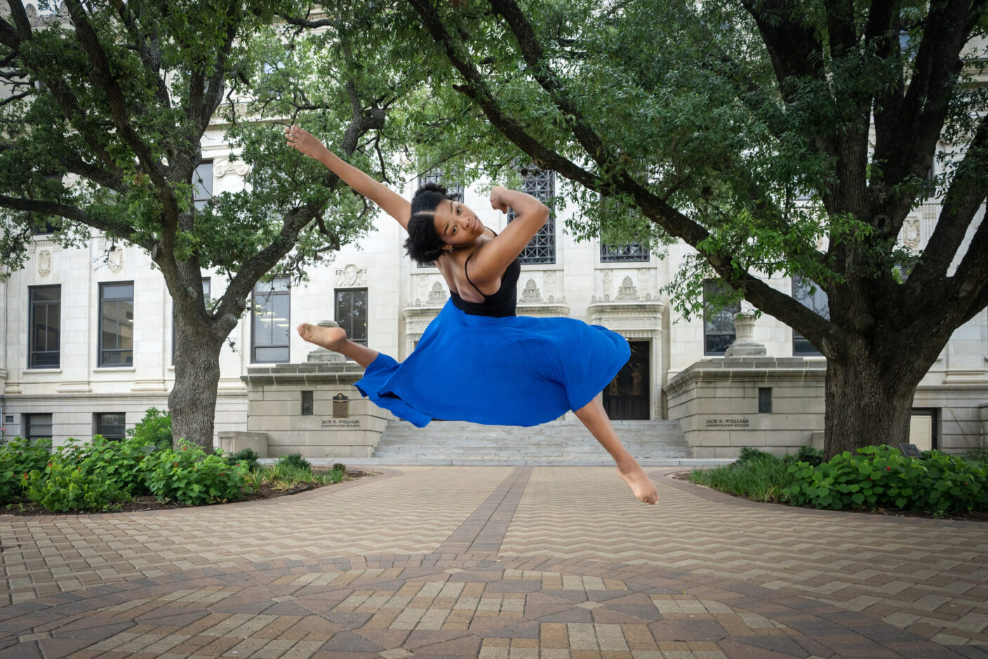 A dancer is in midair as she performs on a university campus setting.