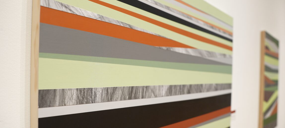 A painting of different colored stripes hangs on a gallery wall.