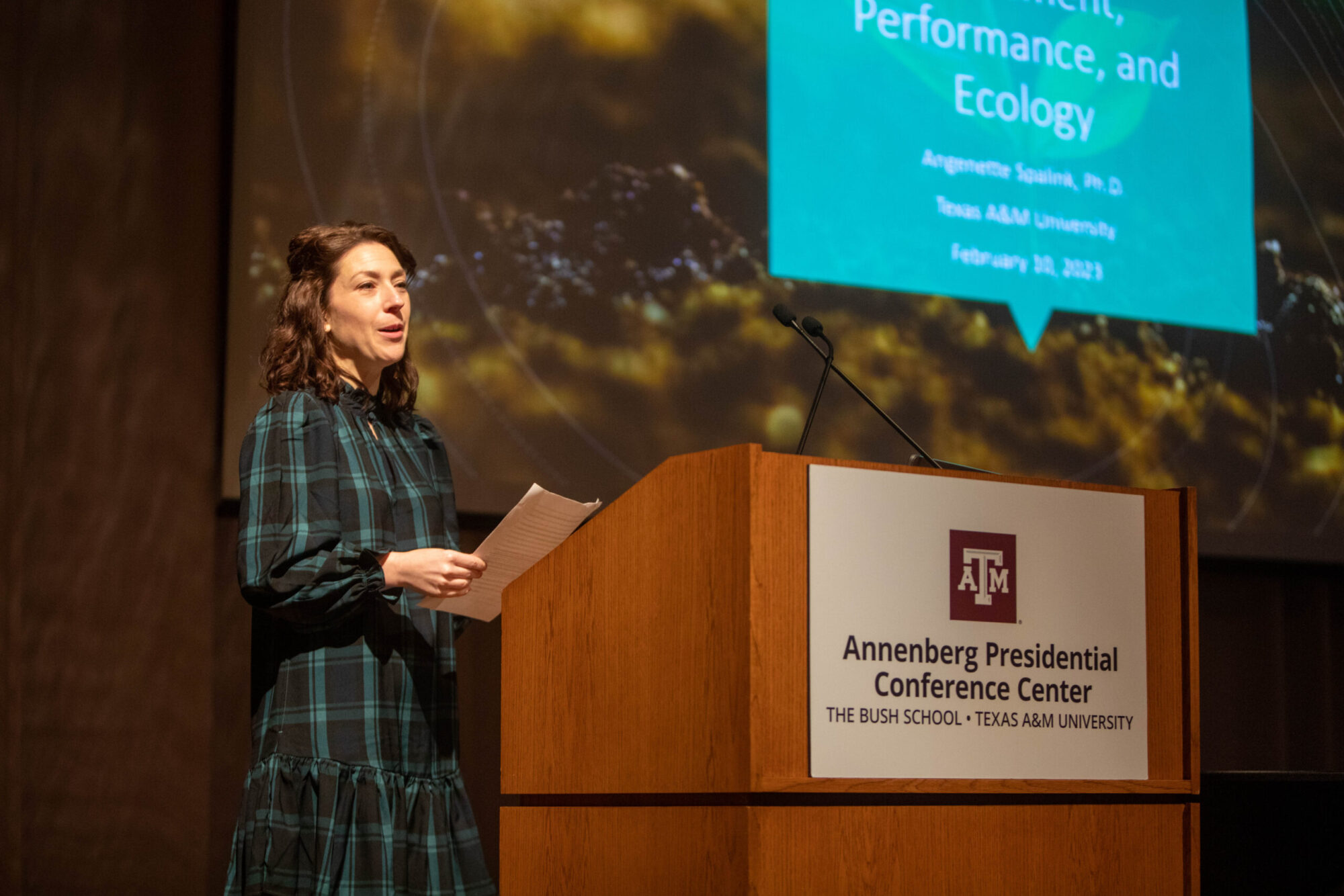 A college professor speaks at a podium that has the Texas A&M logo displayed.