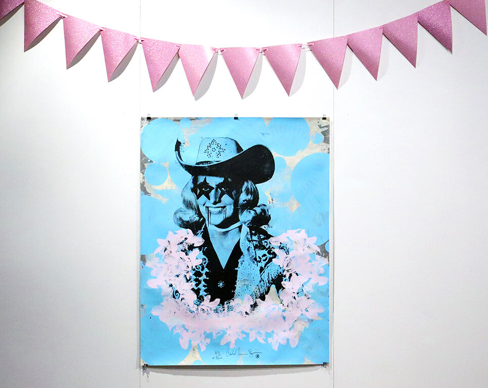 Print art featuring a cowgirl with splotches around her, above the painting is a pink ribbon banner on display in an art gallery.