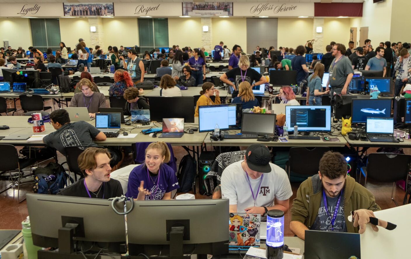A large group of college students are shown looking at their laptops and discussing video game design at the Chillenium game jam.