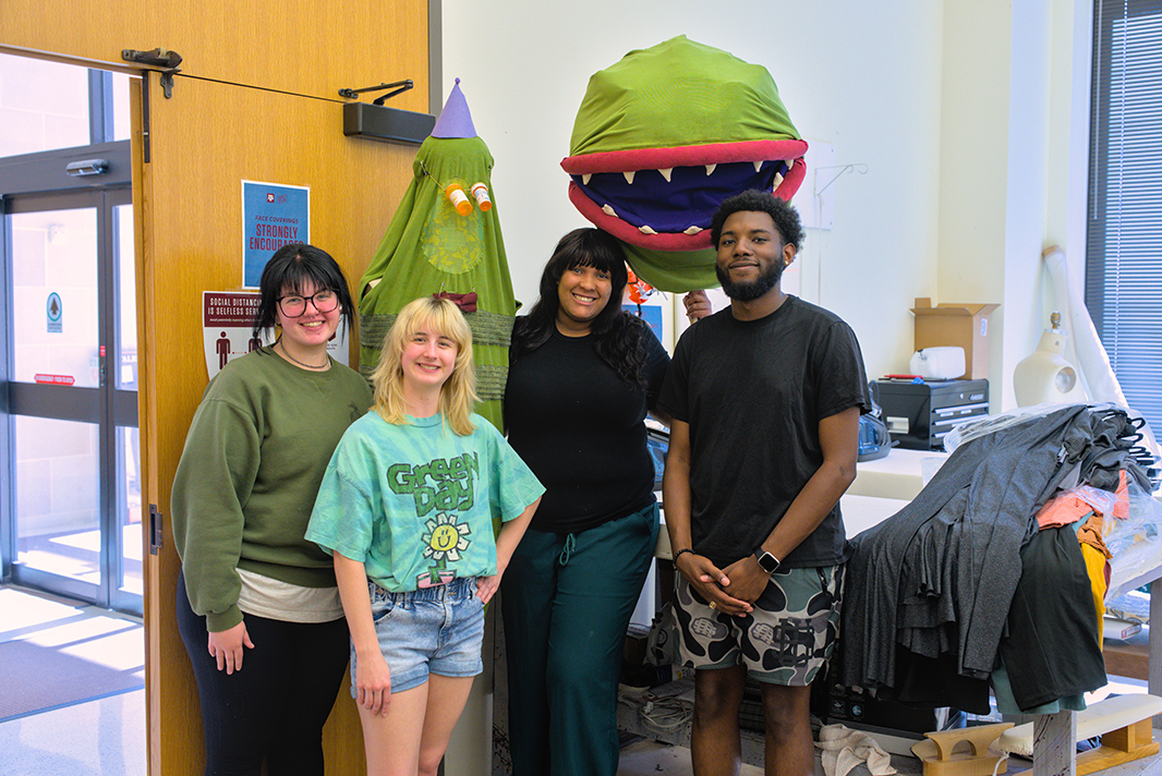 A costume shop manager stands with three college students, with two of their costume character creations behind them.