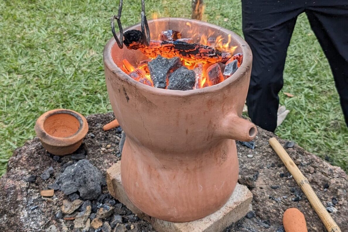 A guaira, with charcoal and flames, is shown as a person works with it with a long pair of tongs.