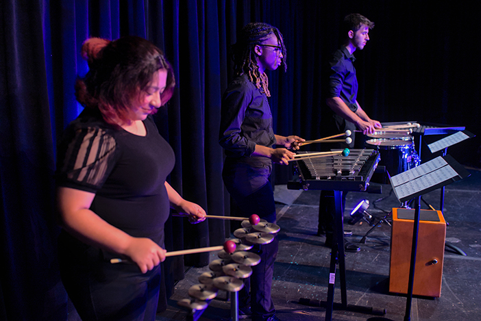 Three college students play percussion instruments.