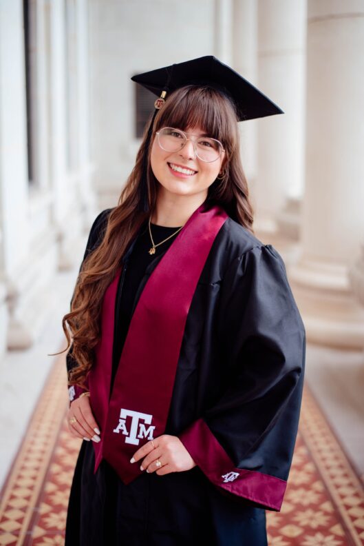 A college student wears a black graduation cap and gown and a mortar board.
