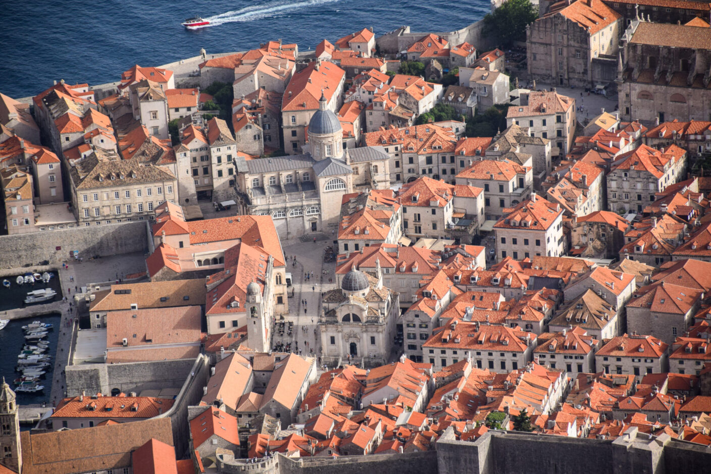 An aerial photo of Dubrovnik, a seaside city in Croatia. The water off the coastline is visible at the top of the image, where a boat can be seen zooming past.