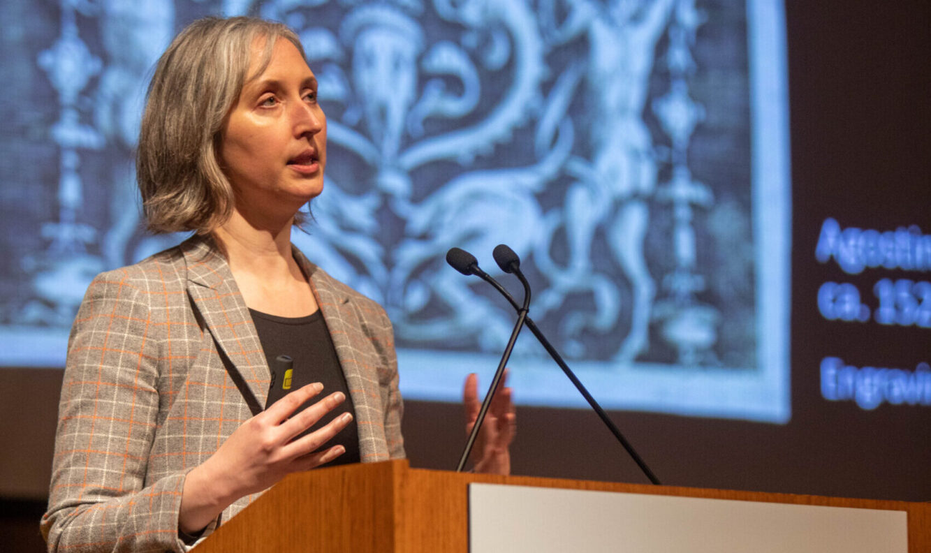 A woman stands at a podium giving an academic presentation