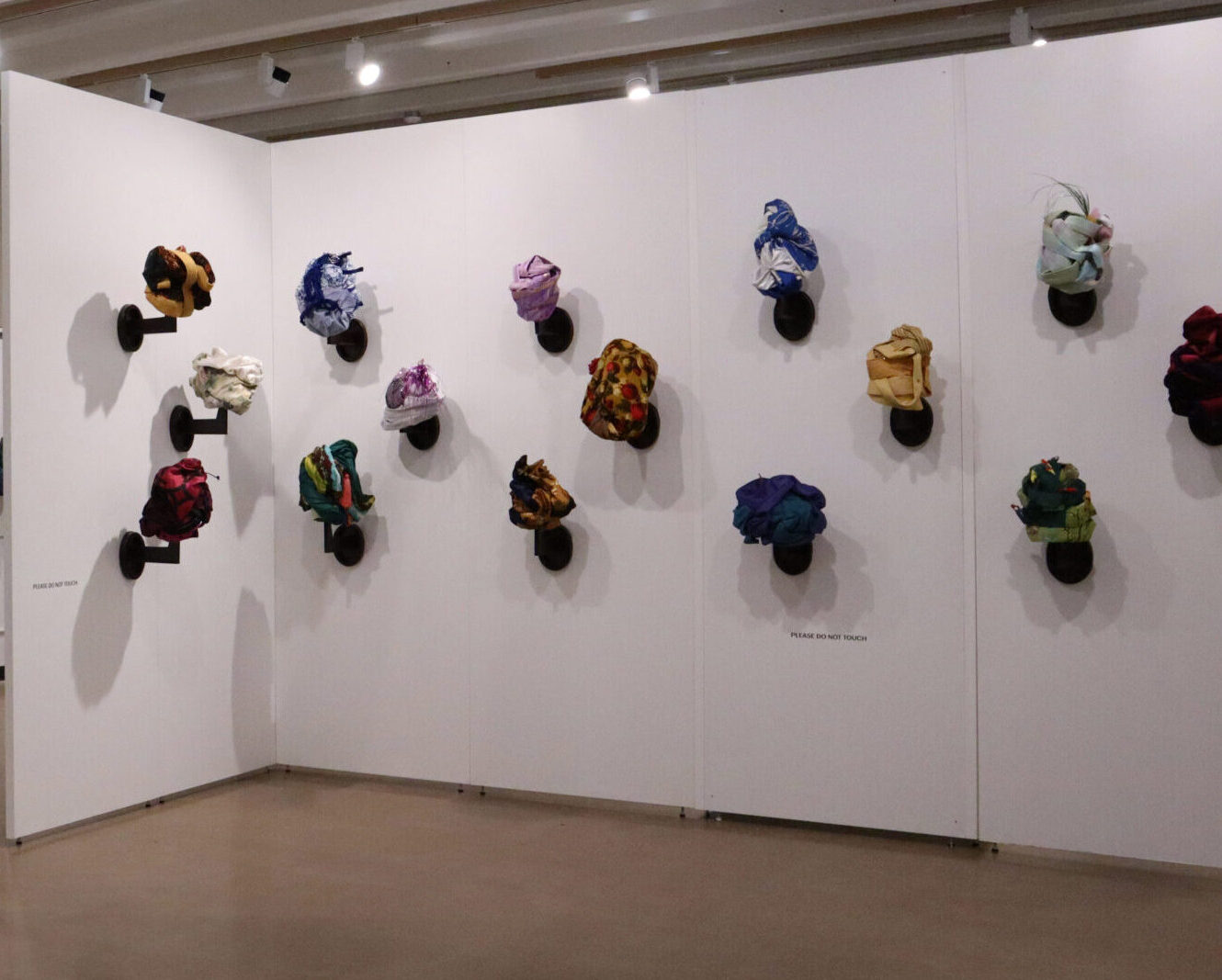 A range of tignon's on display on a wall in an art gallery.