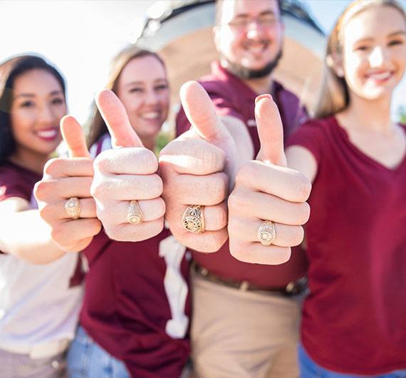 Four students doing a thumbs-up with their right hands lined-up next to each other. All four of them have an Aggie ring on their ring finger.