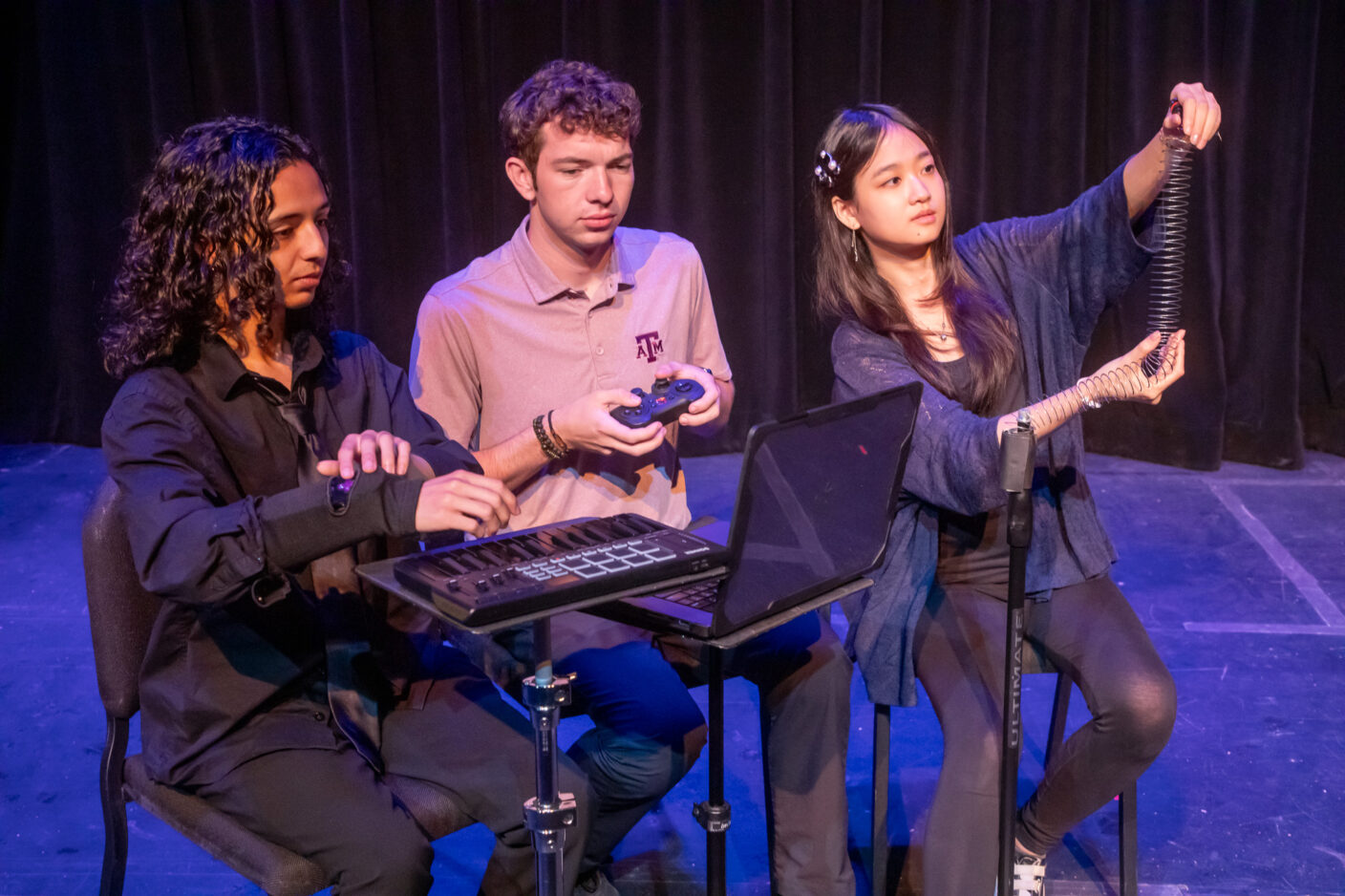 Three college students play experimental music. Two of them are looking at a laptop computer.